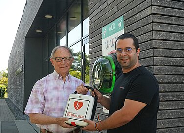 Dritter Bürgermeister Anton Gollmitzer (links) und SIMple-medics-Geschäftsführer Fabian Lindinger präsentieren den neuen Defibrillator am Eingang zur Bruno-Merk-Sporthalle Foto: Michael Lindner/Stadt Günzburg