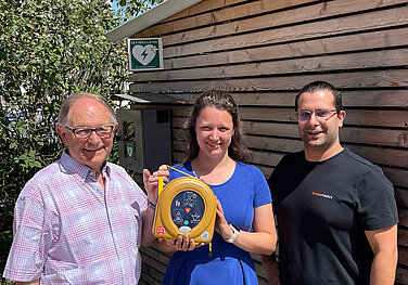 Dritter Bürgermeister Anton Gollmitzer (links), Ständige Vertreterin der ADBV-Leitung Anna Guggemos und Fabian Lindinger, Geschäftsführer von SIMple medics, zeigen den Standort eines neuen Defibrillators in Günzburg. Foto: Michael Lindner/Stadt Günzburg