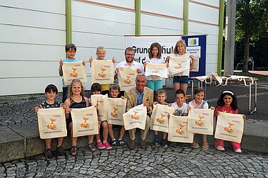 stadt_guenzburg_unterstuetzt_lesefoerderung_mit_buechertaschen Bereits im Juli dieses Jahres überreichte Oberbürgermeister Gerhard Jauernig (unten) den Schülerinnen und Schüler der Grundschule auf der Bleiche anlässlich der Wiedereröffnung der schuleigenen Bücherei Büchertaschen. Die Kinder und Stadtrat Stefan Baisch (oben), damals noch Lehrer an der hiesigen Schule, freuen sich sichtlich über die Taschen.